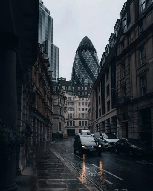 Rain-soaked London street leading toward distinctive city architecture